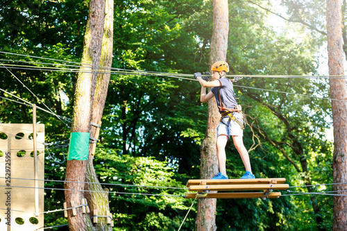 Cute young boy in helmet with climbing equipment in the rope amusement park. Summer camp, holidays concept