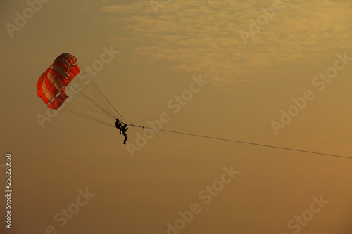 Silhouette of skydiver flies on background of sunset sky and sea