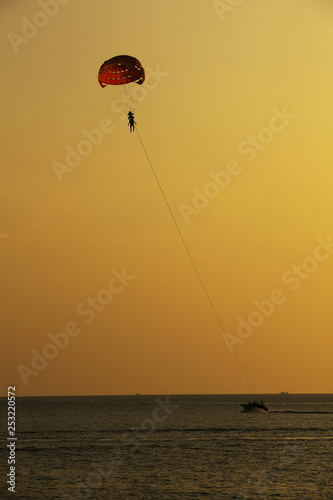 Silhouette of skydiver flies on background of sunset sky and sea