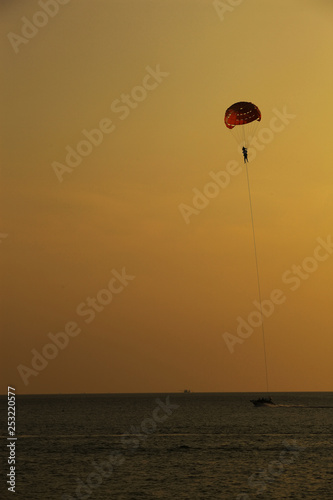 Silhouette of skydiver flies on background of sunset sky and sea
