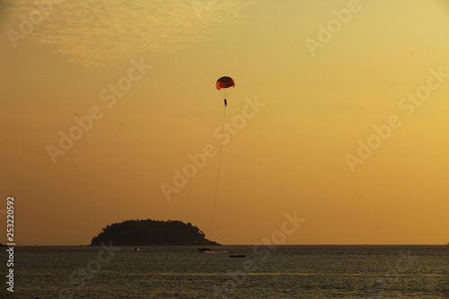 Silhouette of skydiver flies on background of sunset sky and sea