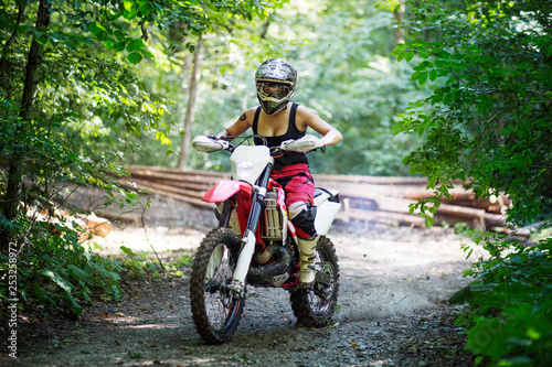 Millennial young woman riding big motocross bike in the forest