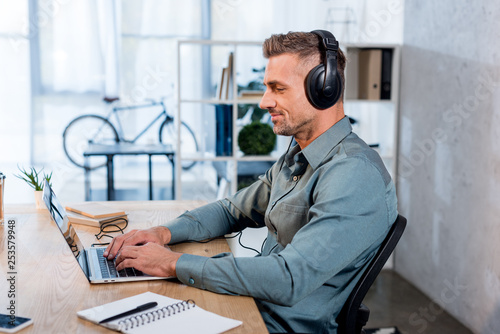 cheerful businessman listening music in headphones while using laptop in modern office © LIGHTFIELD STUDIOS