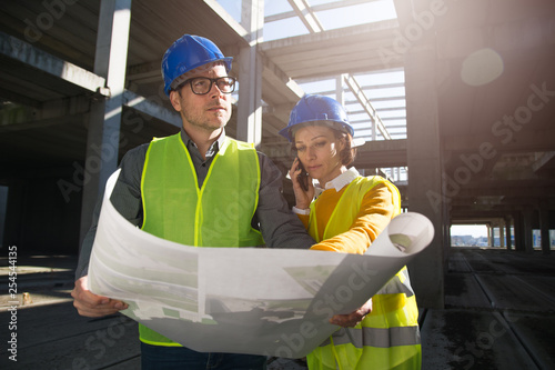 Two young engineers on a construction site, discussing project details