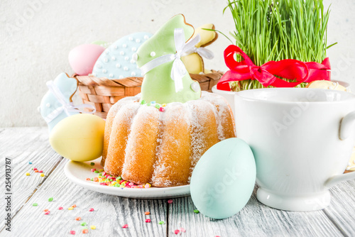 Easter table setting concept, festive table with decoration of young grass, cake, pastel colored eggs, homemade cookies in shape of eggs, bunny rabbits. On a wooden background, copy space © ricka_kinamoto