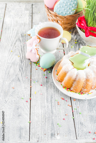 Easter table setting concept, festive table with decoration of young grass, cake, pastel colored eggs, homemade cookies in shape of eggs, bunny rabbits. On a wooden background, copy space © ricka_kinamoto