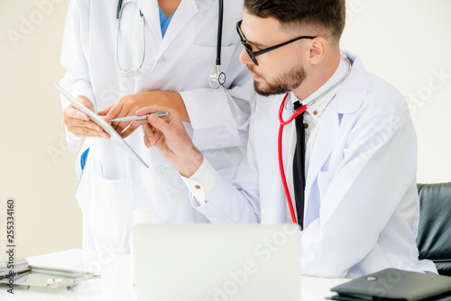 Doctor at hospital office working on laptop computer on the table with another doctor having discussion about patients health.