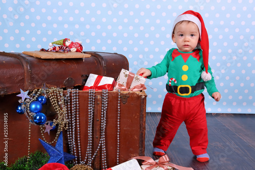 A small boy dressed up as an elf stands in Christmas decorations. © fotodrobik
