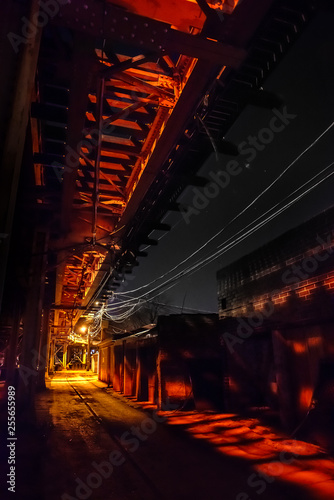 Scary urban city alley with elevated illuminated vintage railway tracks at night in Chicago