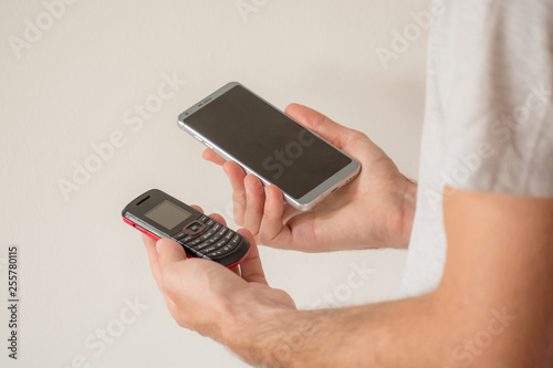 Male hands holding a new smart phone and an old cellphone, on white background. Planned obsolescence concept, technology development, history of communications, millenial devices