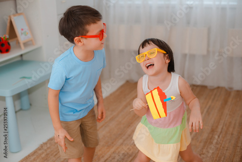 boy and a girl playing with props paper cake with a candle. Children's performance of biting the cake together on their birthday.