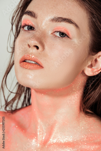beautiful young woman with coral glitter makeup looking at camera isolated on grey © LIGHTFIELD STUDIOS