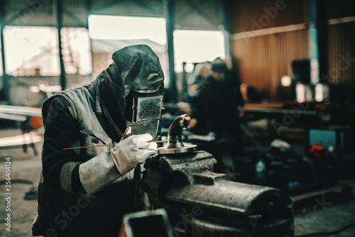 Iron worker in protective suit, mask and gloves welding pipe. Workshop interior. © dusanpetkovic1