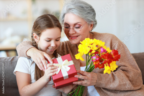 mother's and grandmothers day! family granddaughter congratulates her grandmother on holiday and gives flowers and gifts. © JenkoAtaman