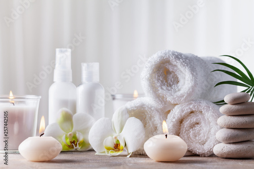 Aromatherapy, spa, beauty treatment and wellness background with massage pebbles, orchid flowers, towels, cosmetic products and burning candles. © juliasudnitskaya