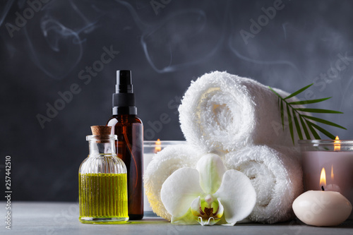 Aromatherapy, spa, beauty treatment and wellness background with massage oil, orchid flowers, towels, cosmetic products and burning candles. © juliasudnitskaya
