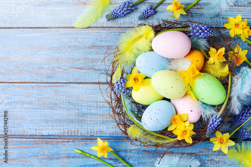 Easter background with colorful eggs in nest, feather and spring flowers top view. Holiday card or banner. © juliasudnitskaya