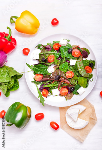 Salad in a white plate, cheese and vegetables on a white wooden background © Katerina