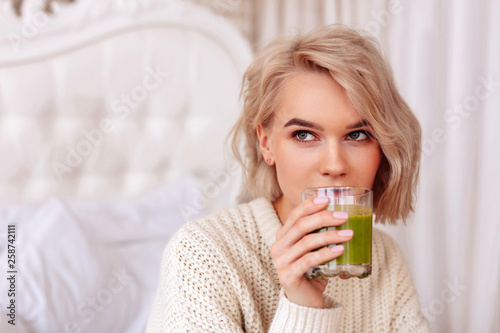 Blonde-haired woman drinking healthy green juice in bedroom © zinkevych