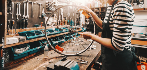Cute Caucasian female worker holding and repairing bicycle wheel while standing in bicycle workshop. © dusanpetkovic1