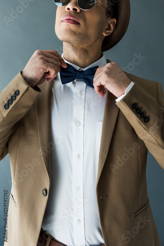 partial view of stylish mixed race man in suit adjusting bow tie isolated on grey © LIGHTFIELD STUDIOS