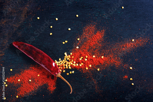 Red Chili pepper flakes and chili powder burst on black background © Niks Ads