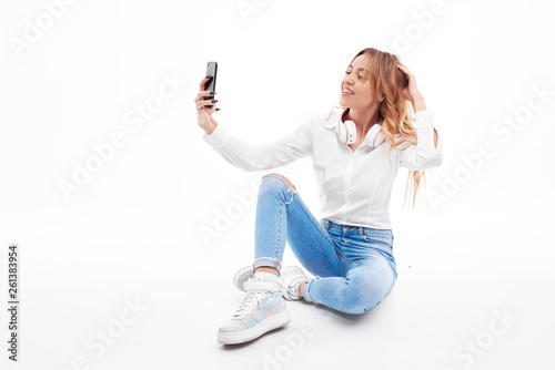 Cheerful young woman with earphones listening to music and talking selfie over white background © shcherban
