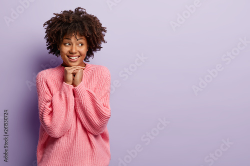 Waist up shot of good looking smiling teenage girl keeps both hands together under chin, focused away, feels shy, gets compliment from stranger, looks with delighted expression. Human emotions © Wayhome Studio