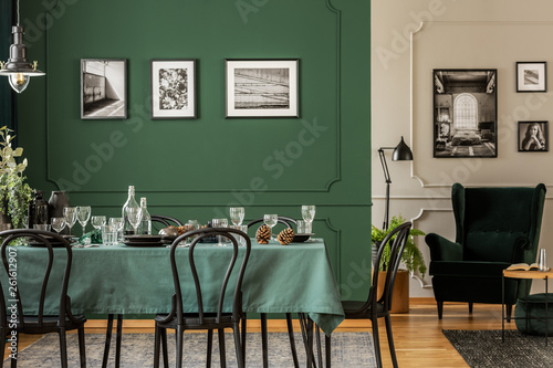 Black and white posters on green wall of stylish dining room interior with log table with wine glasses, plates and cones © Photographee.eu