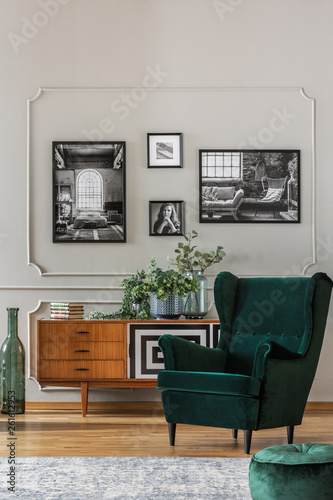 Emerald green armchair in elegant living room with black and white photos on grey wall and retro cabinet © Photographee.eu