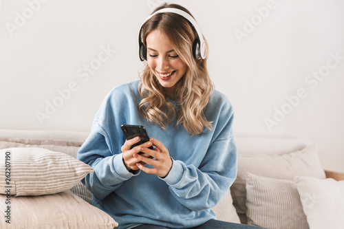 Portrait of attractive blond girl 20s wearing headphones using smartphone and listening to music at home © Drobot Dean