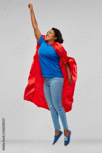 super power and people concept - happy african american young woman in superhero red cape flying up over grey background © Syda Productions