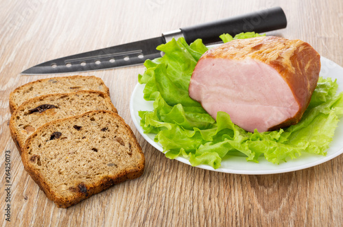 Smoked pork neck with leaves of lettuce in plate, knife, pieces of bread on table © Evgeny