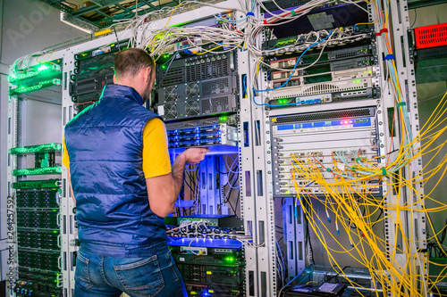 Man works in a server room with lot of fiber optic wires. Engineer replaces computer equipment in data center. Specialist maintains a modern hosting site. System administrator installs a new server. © Климов Максим