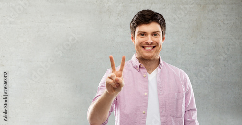 gesture, count and people concept - smiling young man showing two fingers or peace hand sign over grey background © Syda Productions